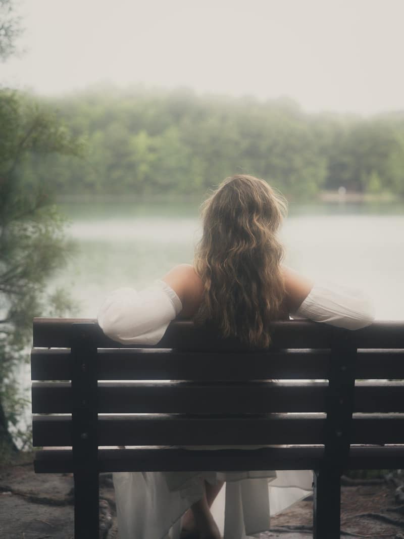 Quiet figure on a bench facing a misty lake