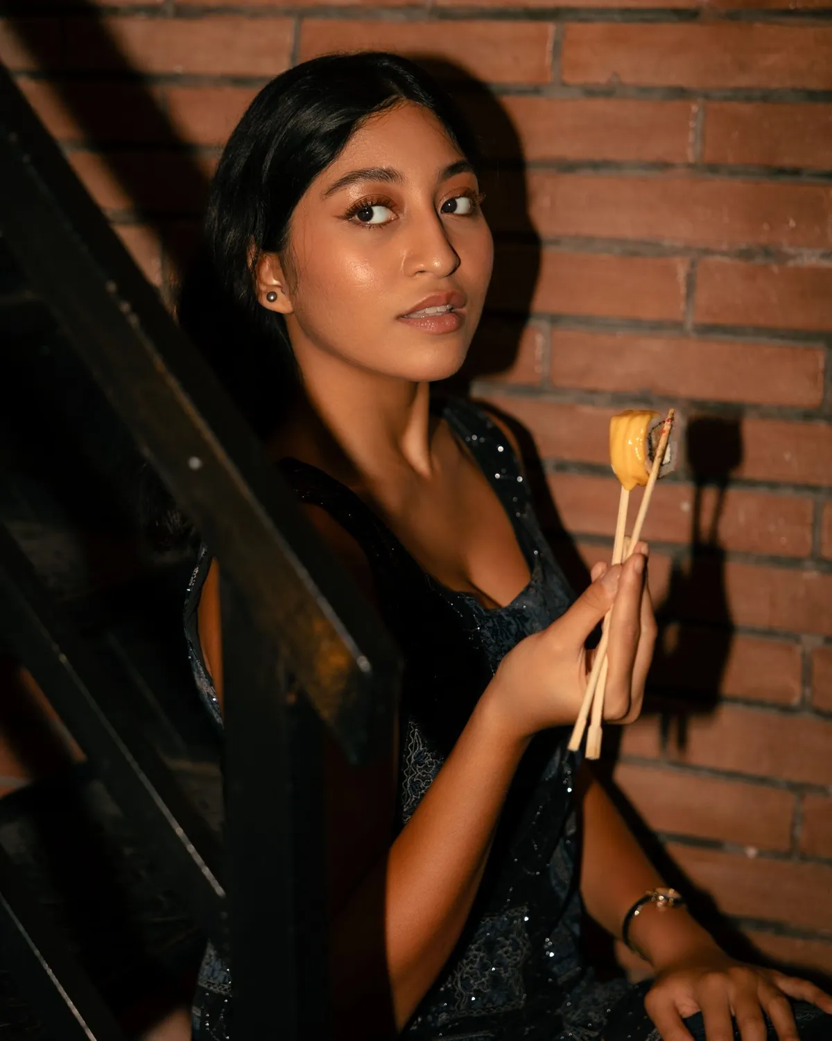 Restaurant guest holding chopsticks beside a brick wall · Friends Sushi