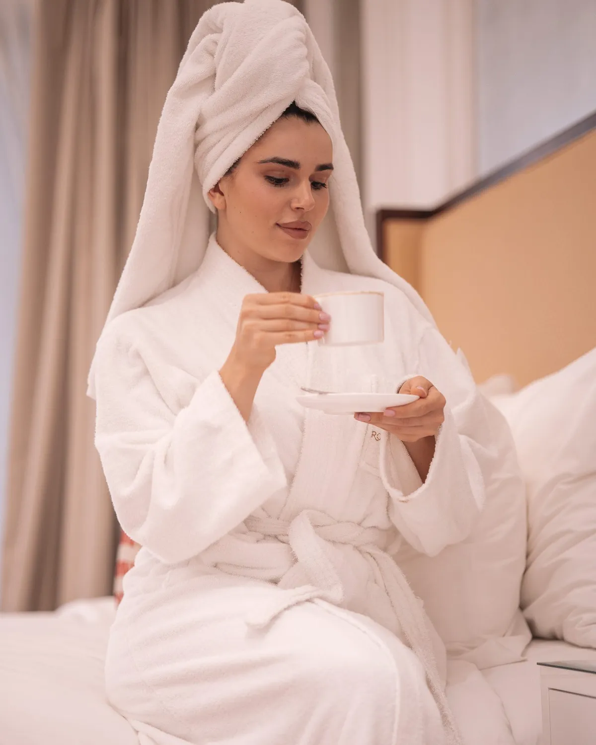 Guest in a robe and towel holding a cup indoors · Royal Saray and Palavra