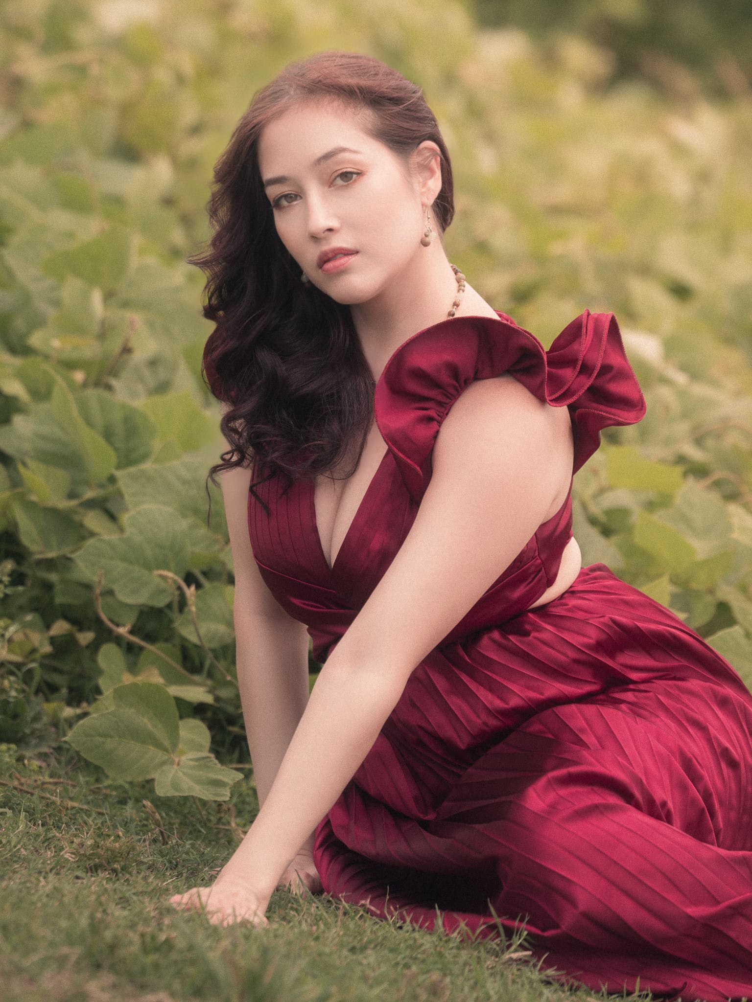 Seated in a kudzu meadow in a wine satin gown